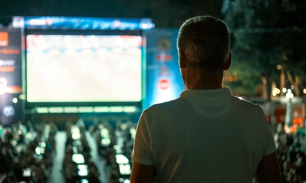 Sitting man watching football in a public place at night